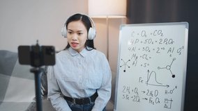 Asian woman chemistry teacher makes a lesson online, live broadcast of the learning process using a smartphone, school lessons and remote work in the context of the coronavirus pandemic.