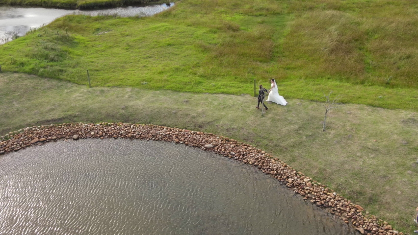 Bride and groom walking alongside pond shot from high angle