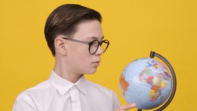 Schoolboy Holding Earth Globe Pointing Finger Choosing Destination, Yellow Background