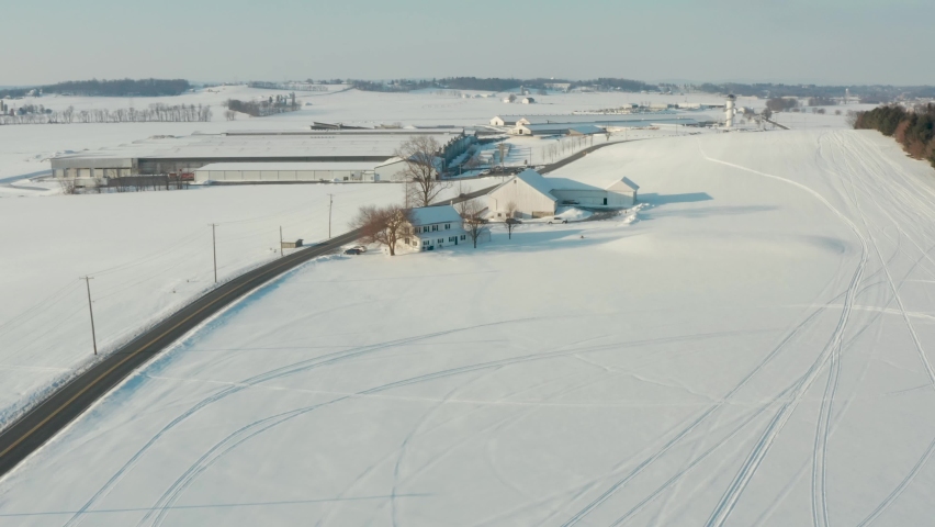 Aerial of farm buildings and fields covered in white winter snow in United States of America, USA. Rural agriculture scene.