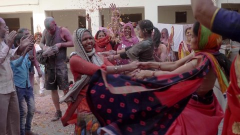 Two happy women in traditional saree are performing spinning dance also known as 'Fugdi' locally are surrounded by people celebrating Holi festival with colours, Vrindavan, India (March 2020) 
