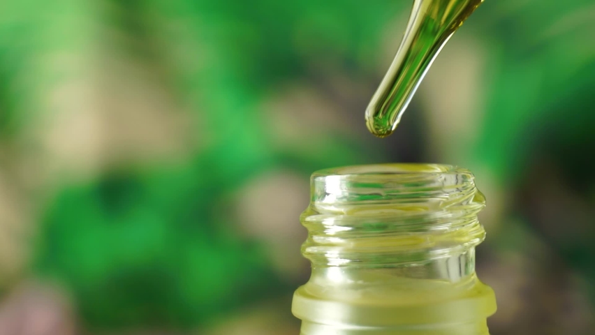 Cosmetic oil drips from a pipette into a glass bottle against a background of blurred green leaves. The drop shows the reflection of green leaves. Hemp oil dripping from a dropper. | Shutterstock HD Video #1069139608