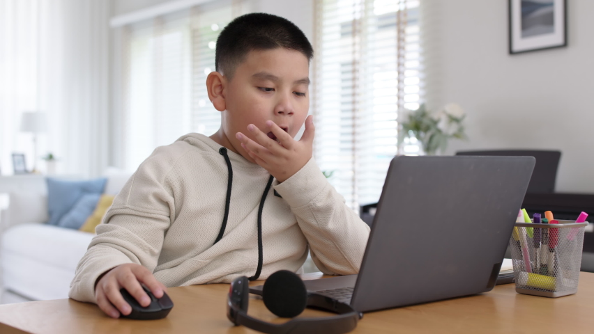 Young asia boy kid sit on desk look at computer notebook feeling bored tired and sleepy in remote learning loss online problem at home distant e-learning primary school class room challenge concept. Royalty-Free Stock Footage #1069139650