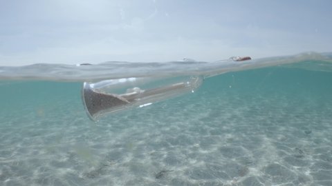 glass bottle with message floats in transparent water of sea or ocean. rolled sheet of paper inside sealed bottle with cork sways on waves against sky.