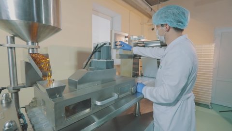 Worker with mask on his face. Mechanism for the production of gelatin-coated tablets. A man in a protective mask and a gown at a drug production facility.