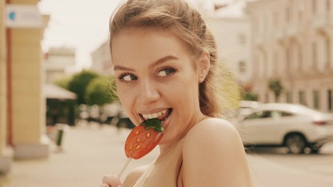 Portrait of beautiful cute model in summer hipster jeans jacket clothes. woman eating lollipop watermelon candy. Woman posing on the street background. Female outdoors