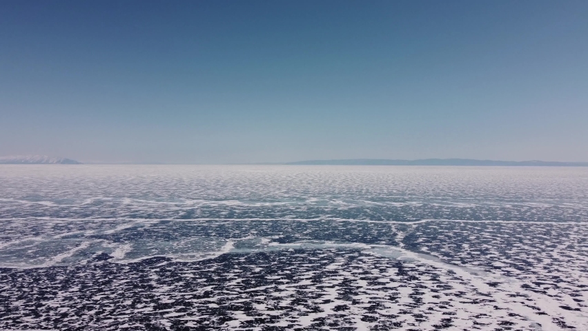 Drone flight over frozen ice of Baikal Lake in Siberia, Russian. Aerial view footage of clear craked ice surface in cold winter day.
