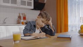 Little boy studying at the table at home. The little boy is writing in his notebook.Distance education concept. Slow motion video. 	