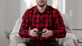 Young unrecognizable bearded man using game controller indoors. Concentrated Caucasian male gamer playing video game at home. Competition and leisure concept.
