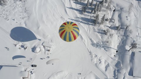 AERIAL: landing of a paraglider with a passenger on a ski slope, next to a large beautiful balloon. snow-covered forest on a sunny day. 4k Prores 422