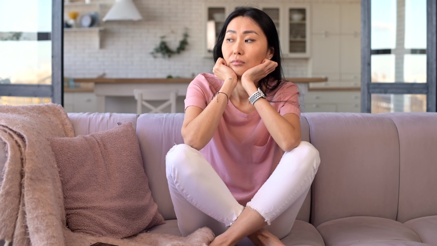Young adult Asian mixed-race female domestic housewife with long black hair sitting on the couch, feeling bored and demotivated, does not want to do tasks, upset with the message from phone, unhappy Royalty-Free Stock Footage #1069171651