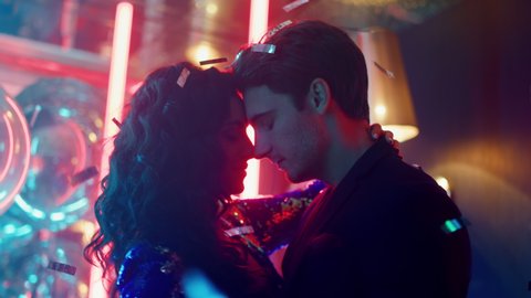 Love couple touching foreheads in nightclub. Sexy people moving bodies at night club party. Young man and woman laughing on neon lamps background.