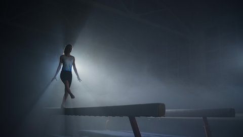 graceful young female gymnast is performing on balance beam, training in sport school, youth and sport activities, slow motion shot