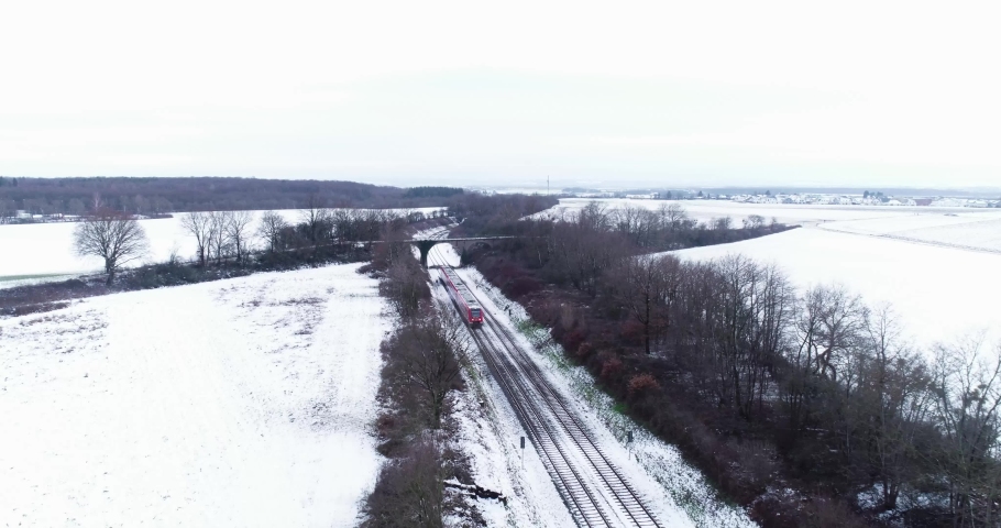 Aerial Red Commuter Train close in scenic white snowy winter wonderland landscape bridge forest Royalty-Free Stock Footage #1069176724