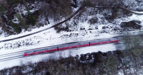 Aerial Birds Eye of Red Commuter Train in scenic white snowy winter wonderland landscape bridge forest