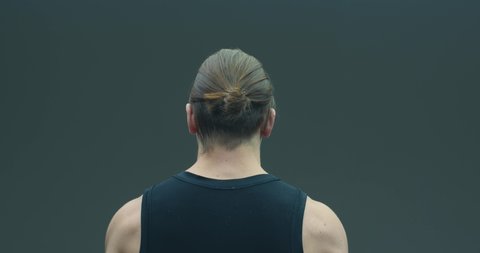 Video of long haired guy letting down his hair on gray studio background. Back view. Haircare concept. Ad of shampoo