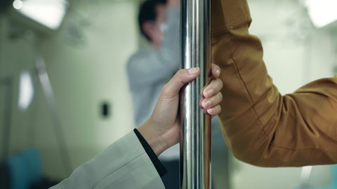 The hand of a man harassing a woman's hand clinging to a rail on a public transportation system at night