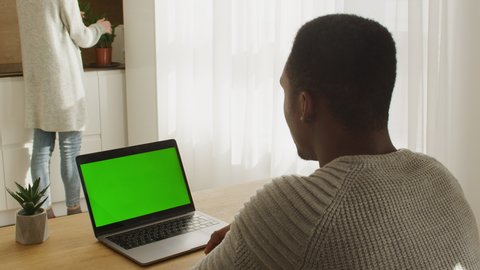 Young mixed-race couple in their apartment with an african american man sitting in front of a green screen laptop on a video call