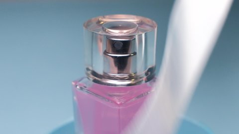 A white ribbon swirls beautifully around a bottle of pink perfume and flies away on a blue background