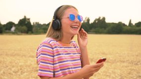 Slow motion tracking video clip of beautiful mixed race African American girl teenager young woman wearing a red and black shirt and blue sunglasses walking listening to music on wireless headphones 