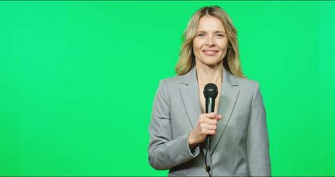 Beautiful female news TV presenter telling positive news smiling holding microphone on green screen background. Concept of breaking news.