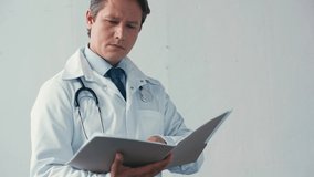 serious doctor in white coat looking at folder on grey
