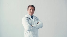 doctor in white coat with stethoscope standing with crossed arms on grey