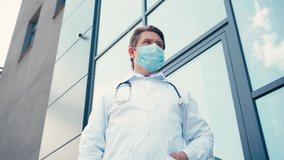 low angle view of doctor in medical mask standing with crossed arms outside