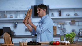 excited man dancing with spice mills near table with fresh ingredients