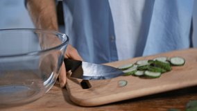 cropped view of man adding sliced cucumber into glass bowl