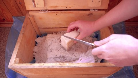 A hand opens a wooden box in which lard is salted, covered with gauze and cuts off a piece of salted lard