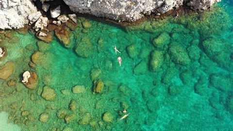 Aerial view of a young couple snorkeling above coral reef reaching deeper parts of the crystal clear water, Rhodes, Greece. Aerial drone view of a couple snorkeling swimming in crystal clear water.