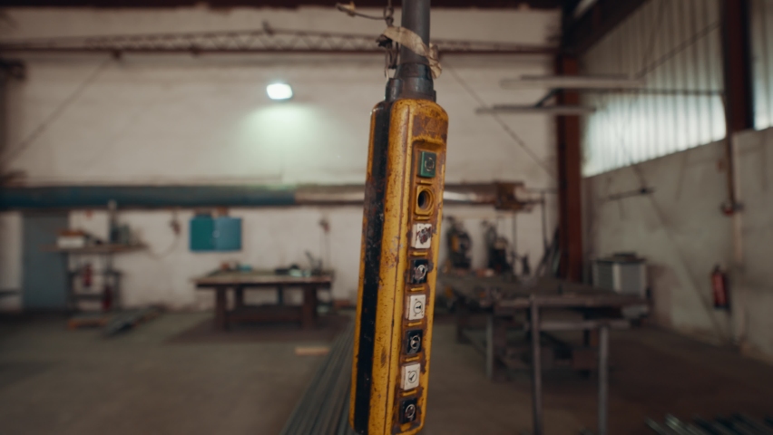 Crane remote hanging in the air in a warehouse, metal workshop. 4K 50fps slow motion