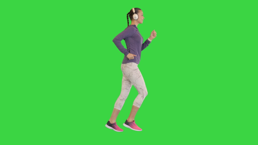 Wide shot. Side view. Healthy beautiful girl jogging and listens to music with headphones on a Green Screen, Chroma Key. Professional shot in 4K resolution. 068. You can use it e.g. in your medical,