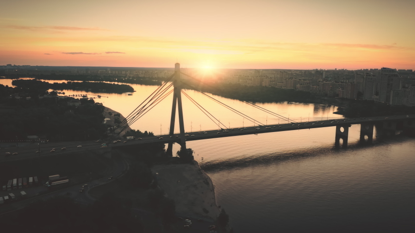 Sunset across river bridge traffic road aerial. Cars, trucks ride on highway. Summer nobody nature landscape. Cityscape. Urban transportation. Buildings at sun set. Dnieper, Kiev town, Ukraine, Europe