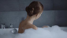 beautiful young woman washing shoulder and looking at camera in bubble bath
