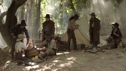 A group of cowboys camps panning for gold on the riverside.