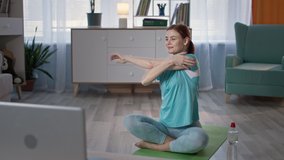 housewife in sportswear doing body workout on yoga mat with online lessons at home during quarantine
