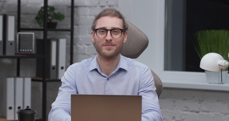 Portrait of Smiling Successful Manager in Eyeglasses at Modern Workplace. Confident Caucasian Man Working Distance at home. Looking at Camera. Quarantine Concept. People. Royalty-Free Stock Footage #1069203487