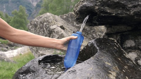 Slow motion: Female refilling reusable plastic bottle from fountain in the mountains 