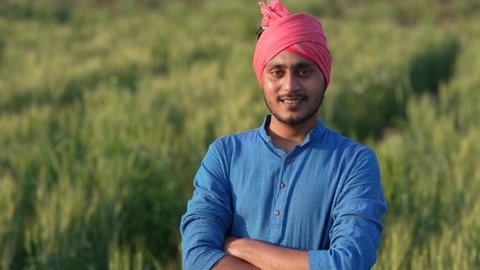 Young indian farmer walking his wheat field and giving happy expression