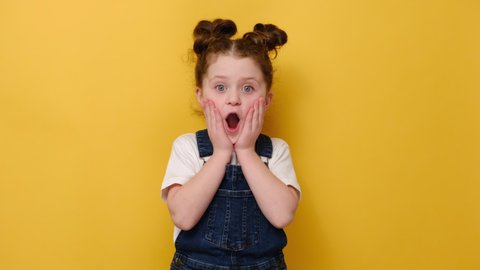 Portrait of surprised little preschool girl look at camera feel stunned amazed by unexpected good news, happy cute small child shocked by unbelievable surprise, isolated on yellow studio background