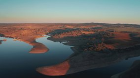 Aerial view of the sun setting beyond the horizon in beautiful countryside area. Rural area with scenic landscape of ponds and clay soil hills in a golden hour lighting. High quality 4k footage
