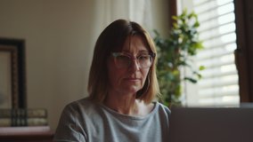 A mature woman looks at the screen and closes the laptop cover. Remote work freelancer at home workplace. An adult woman is completing work on a laptop. High quality 4k footage