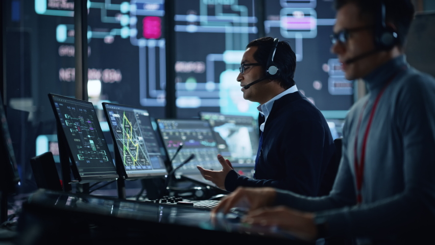 Portrait of Professional IT Technical Support Specialist Working on Computer in Monitoring Control Room with Digital Screens. Employee Wears Headphones with Mic and Talking on a Call. Royalty-Free Stock Footage #1069211353