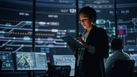 Young Multiethnic Female Government Employee Uses Tablet Computer in System Control Monitoring Center. In the Background Her Coworkers at Their Workspaces with Many Displays Showing Technical Data. - Powered by Shutterstock - Get 15% off with code: PIKWIZARD15