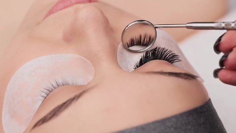 Eyelash extension procedure. Professional beauty master showing results of work in special mirror. Fake eyelashes. Eyelashes extensions close up. Makeup artist and client in beauty salon.