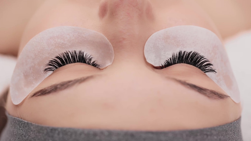 Eyelash extension procedure. Professional beauty master combing female lashes with special mascara brush. Fake eyelashes. Eyelashes extensions close up. Makeup artist and client in beauty salon. | Shutterstock HD Video #1069212136
