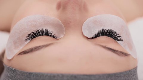 Eyelash extension procedure. Professional beauty master combing female lashes with special mascara brush. Fake eyelashes. Eyelashes extensions close up. Makeup artist and client in beauty salon.
