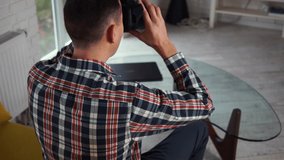 Young modern caucasian man takes off VR-headset. View from the back. Sitting on the couch in a cozy smart apartment near the window. Close-up of VR glasses helmet. Augmented reality - Powered by Shutterstock - Get 15% off with code: PIKWIZARD15